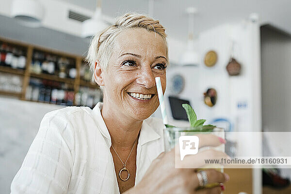 Happy blond woman with cocktail sitting in restaurant
