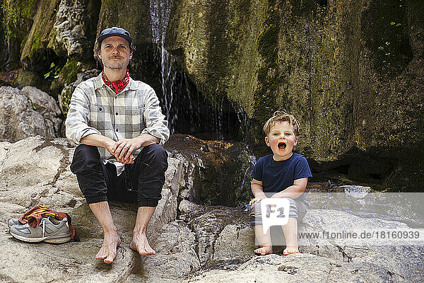 Happy boy with father sitting on rock