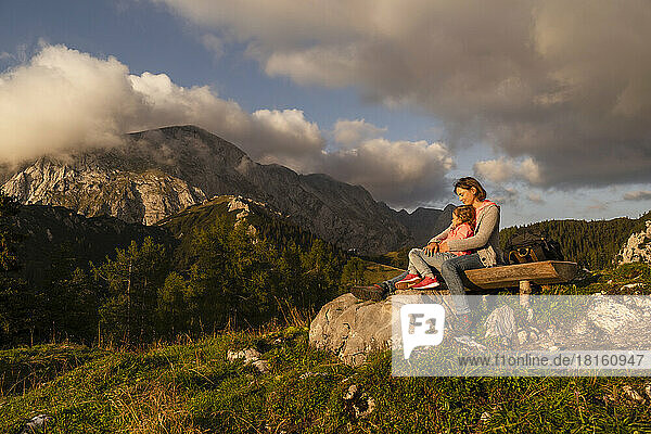 Woman with daughter sitting on bench at sunset