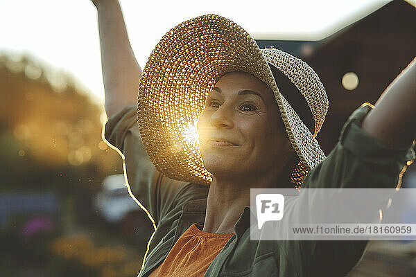 Smiling woman with arms raised wearing hat in garden