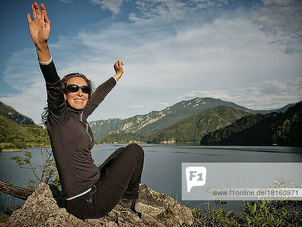 Happy woman with arms raised on rock in front of lake