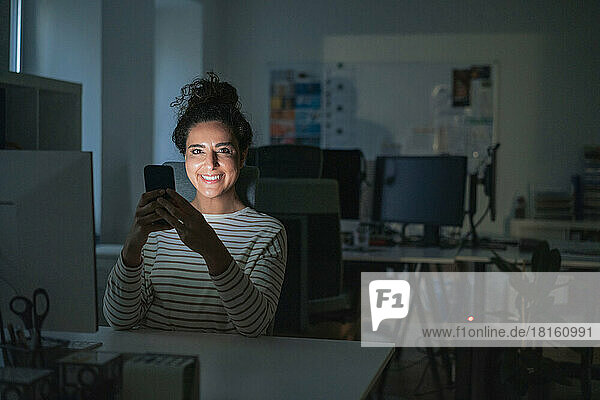 Smiling businesswoman with mobile phone at desk in office
