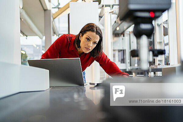 Concentrated engineer with laptop examining machine at factory