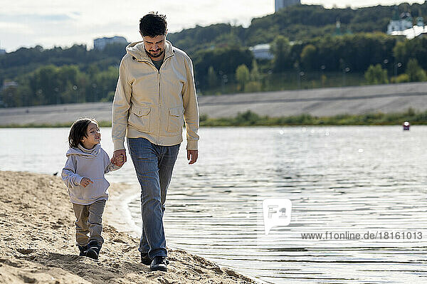 Vater und Sohn gehen gemeinsam Händchen haltend am Fluss entlang