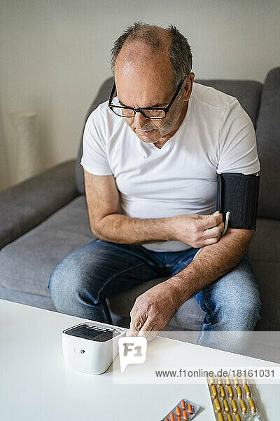 Senior man checking blood pressure through device in living room
