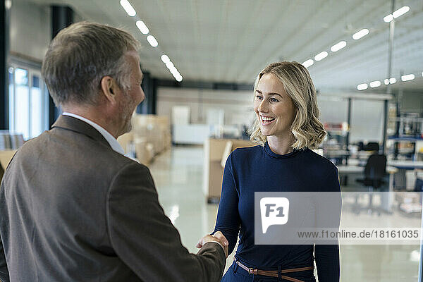 Happy blond businesswoman handshaking with colleague at warehouse