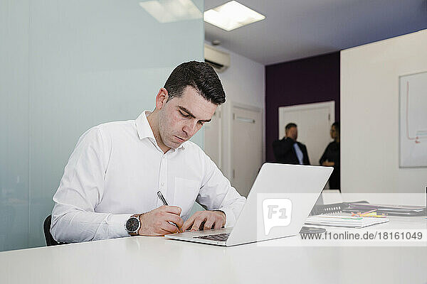 Young businessman writing in front of laptop at desk in office