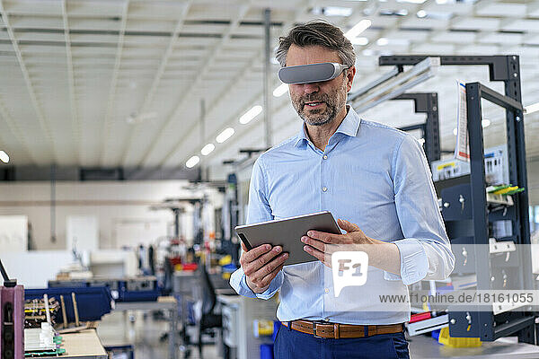 Mature businessman wearing virtual reality simulator holding tablet PC at industry