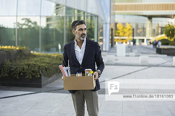 Businessman with office supply in box standing on footpath