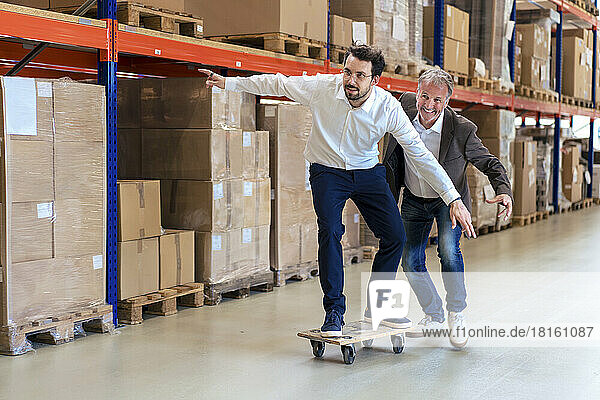 Carefree businessman skateboarding with colleague at warehouse