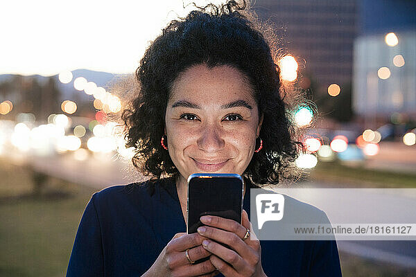 Smiling businesswoman with mobile phone at dusk