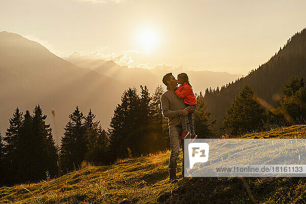 Father kissing daughter on mountain at sunset