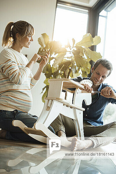 Pregnant woman photographing man repairing rocking horse at home