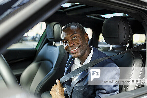 Happy businessman fastening seat belt in car
