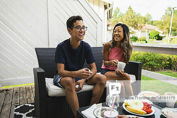 Happy mother and son having snacks sitting on couch at porch