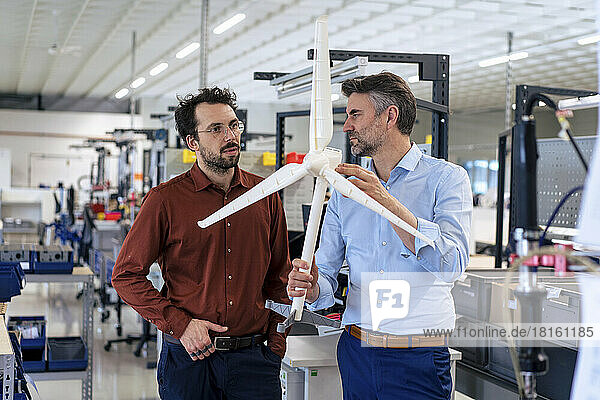 Mature businessman with colleague examining wind turbine at warehouse