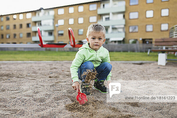 Cute boy splashing sand with shovel in playground
