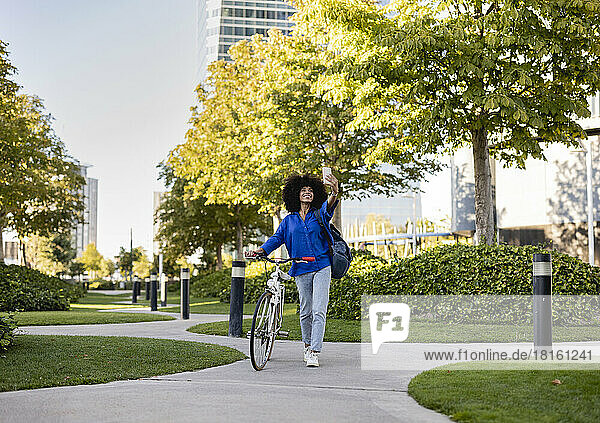 Happy woman with bicycle taking selfie through mobile phone at park