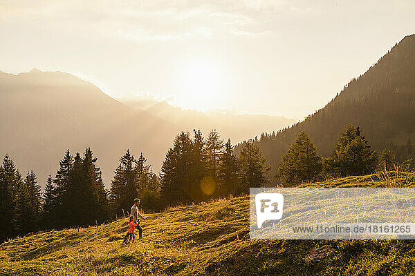 Man with daughter hiking on mountain at sunset