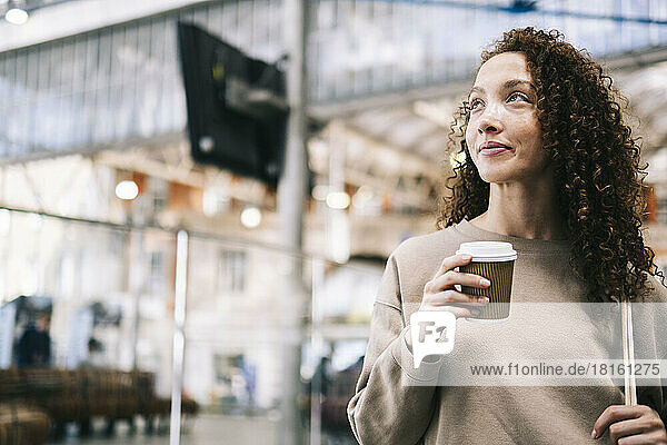 Smiling woman with disposable cup of coffee at train station