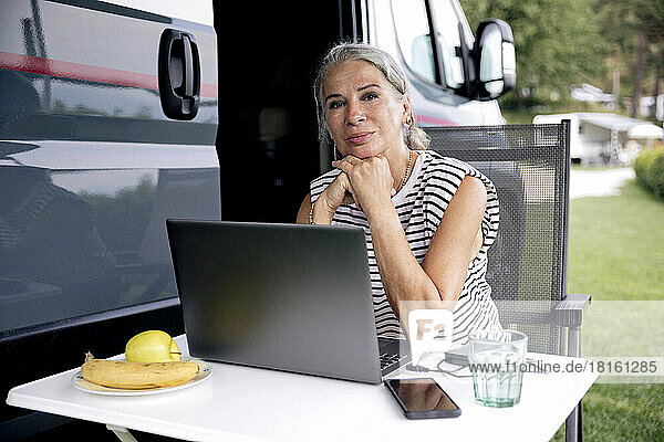Thoughtful freelancer sitting with laptop outside van