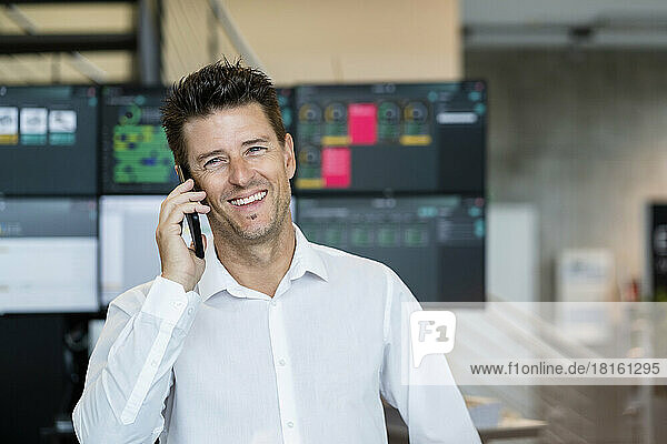 Happy businessman talking on mobile phone in front of computer monitors