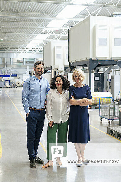 Smiling senior businesswoman with arms crossed standing by colleagues in industry