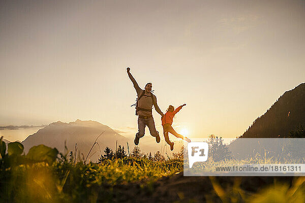 Happy man with daughter jumping on top of mountain