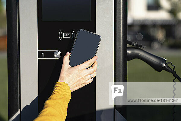 Hand einer Frau  die an der Fahrzeugladestation per Smartphone bezahlt