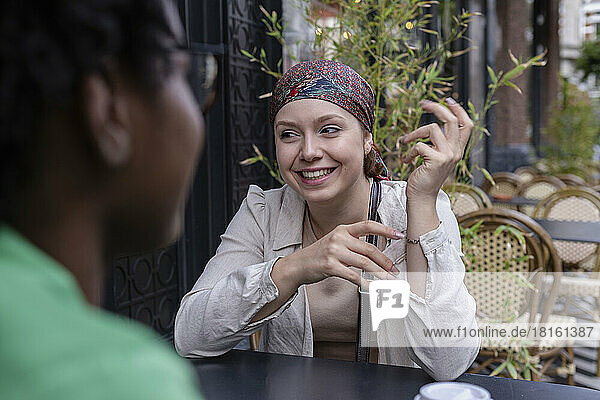 Happy woman wearing bandana talking with friend at sidewalk cafe