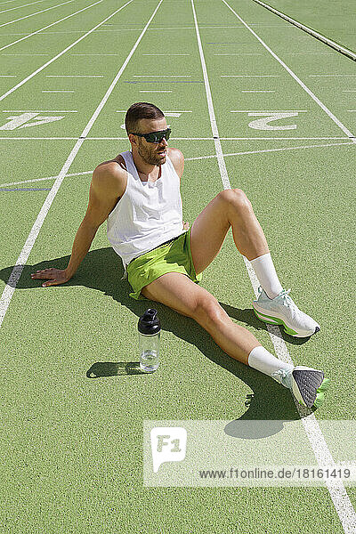 Müder Sportler mit Sonnenbrille entspannt sich auf der Sportstrecke