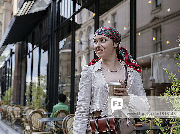 Young woman wearing bandana holding disposable cup at sidewalk cafe