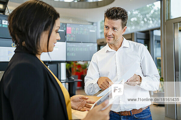 Smiling businessman showing paper to businesswoman holding tablet PC in industry