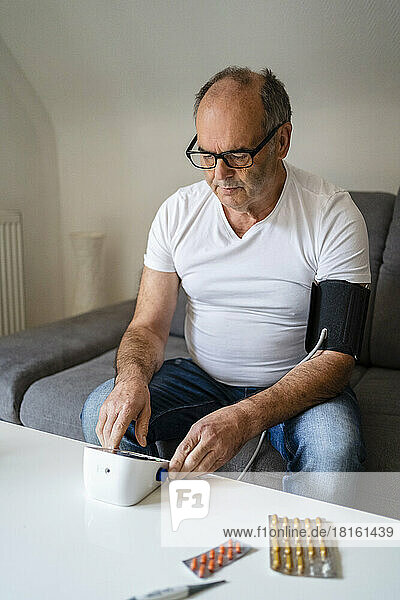 Man measuring blood pressure through device sitting on sofa at home