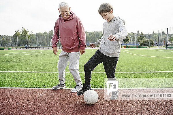 Happy boy with grandfather playing with soccer ball at sports field