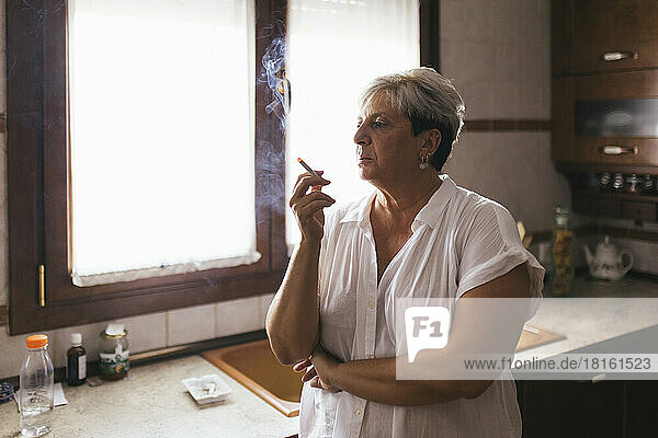 Depressed woman smoking cigarette in kitchen at home
