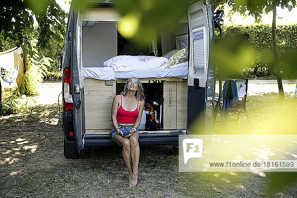 Senior woman sitting with mobile phone on bumper of camper van