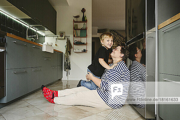 Happy son with mother sitting on floor in kitchen