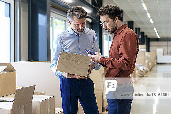 Businessman with colleague examining machine part at warehouse