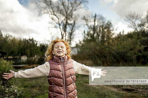 Happy girl standing with arms outstretched in garden
