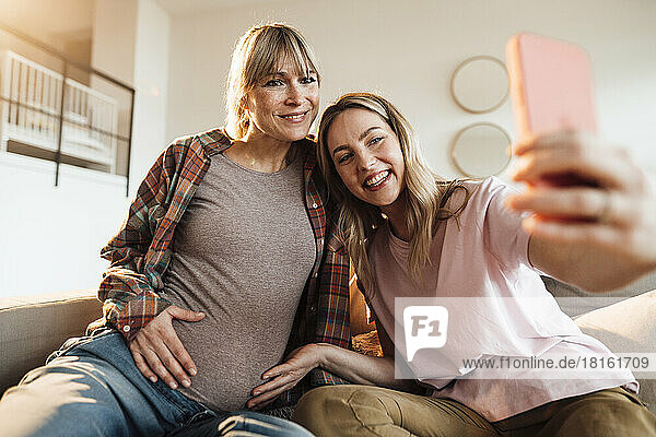 Glückliche Frau  die zu Hause ein Selfie mit ihrer werdenden Schwester per Smartphone macht