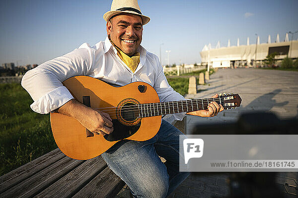 Smiling guitarist playing guitar and recording through smart phone on tripod