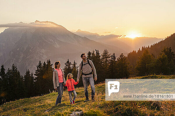 Smiling woman and man holding daughter's hand on mountain