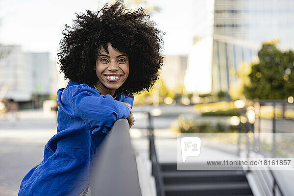 Happy woman with Afro hairstyle leaning on railing