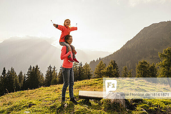 Smiling woman carrying daughter on shoulder at sunset