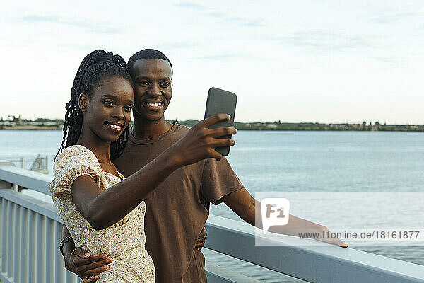 Smiling young couple taking selfie standing by river