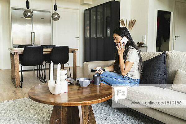 Frau spricht mit Smartphone und sitzt zu Hause auf dem Sofa