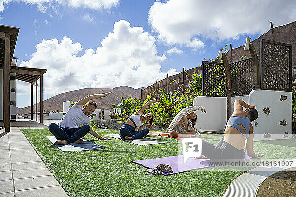 Yoga instructor and multiracial friends stretching on exercise mat in back yard