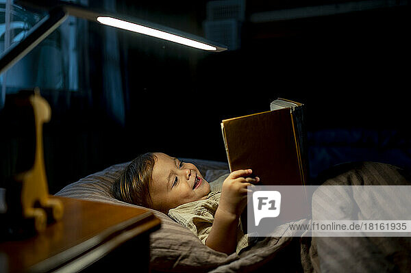 Glücklicher Junge  der zu Hause im Bett liegt und ein Buch liest