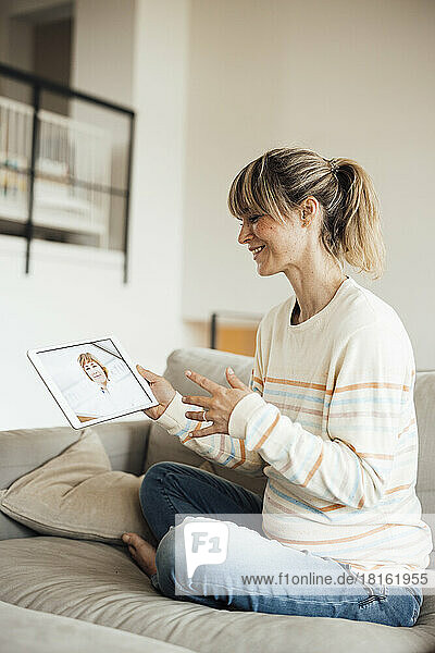 Schwangere Frau macht Online-Konsultation mit Arzt über Tablet-PC auf Sofa sitzend
